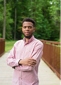 Quentin Sanders wears a pink shirt in his faculty profile standing on Mason's outdoor bridge