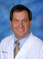 A man wearing a lab coat, blue shirt and striped tie, posing for a portrait photo.