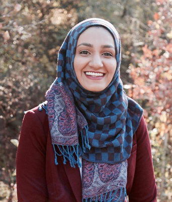 Young, female student wearing a patterned hijab and wine red suit jacket.